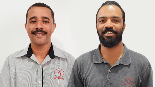 Dois funcionários da PAX Domini sorridentes, vestindo uniformes cinza com o logotipo da empresa, preparados para o serviço de assistência em capela.